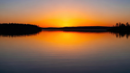 A tranquil lake scene at sunset, featuring a calm body of water reflecting the vibrant hues of the sky, surrounded by silhouetted trees and hills.の素材