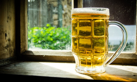 Glass of fresh beer on an old wooden window sill .