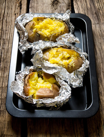 Potato food . Baked potatoes in foil on a wooden table .の写真素材