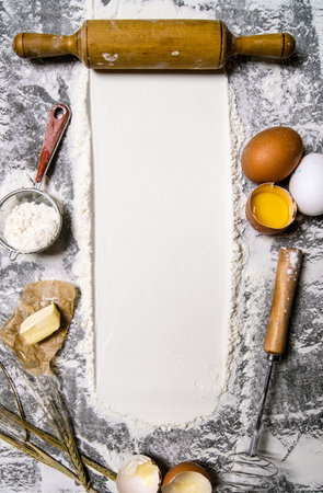Preparation of the dough. The rolling pin with flour and other ingredients for the dough on the stone table. Free space for text. Top viewの写真素材