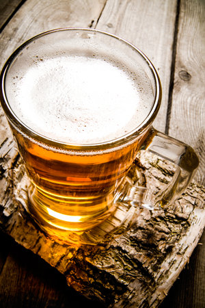 Glass of light beer on a birch stand . On a wooden table.の写真素材