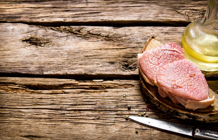 Fresh raw meat with knife and oil on a wooden stand. On a wooden table. Free space for text .の写真素材