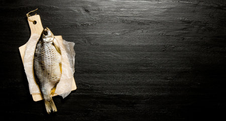 Dried fish on a wooden board. On black chalkboard. Free space for text. Top view