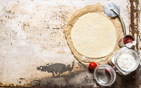 The rolled out pizza dough with flour and tomato sauce. On rustic background. Top viewの写真素材