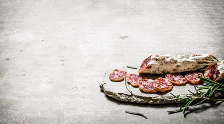 Sliced salami flavored with rosemary and spices. On a stone background.