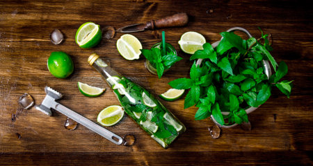 Mojito cocktail. Ingredients for cooking - limes, mint leaves, hammer, rum on the wooden background. Top viewの写真素材
