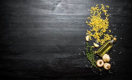 Pasta background. Dry pasta with mushrooms and herbs. On a black wooden background. Free space for text . Top viewの写真素材