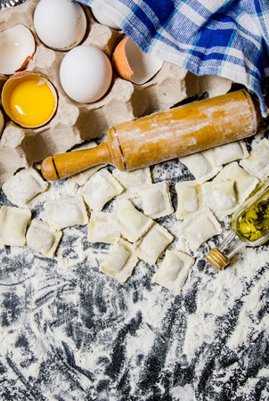 Fresh ravioli with a rolling pin, eggs and olive oil. On black table with flour. Top viewの写真素材