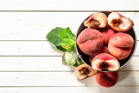 Ripe peaches in a steel bucket. On a white wooden table.の写真素材