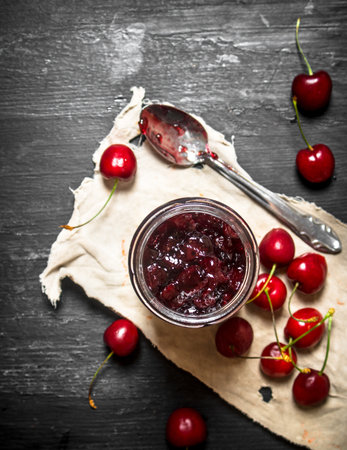 Cherry jam in a jar on the old fabric. On a black wooden background.の写真素材