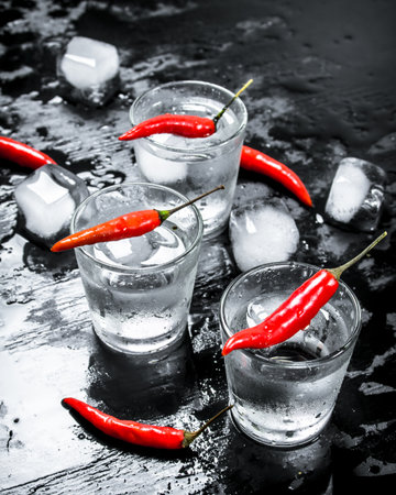 Vodka shots with hot chili peppers and ice. On the black chalkboardの写真素材