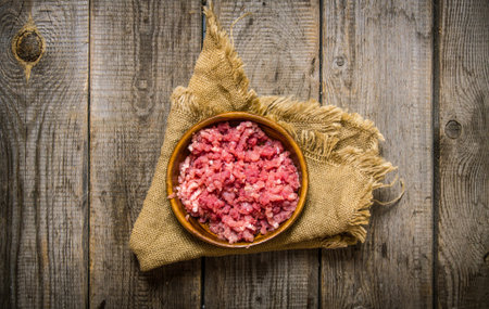 Raw minced meat in a wooden bowl on old fabric. On a wooden table. Top view