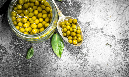 Marinated green peas in glass jar. On a rustic background.