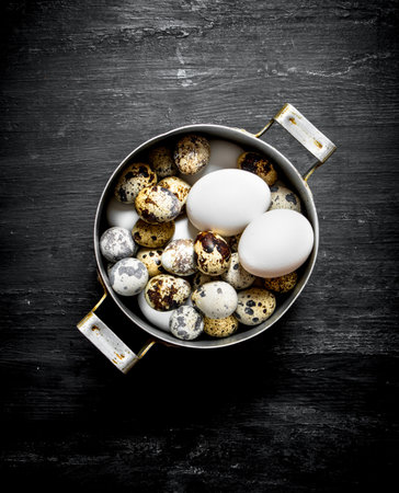 Quail and chicken eggs in an old pot. On a black wooden background.の写真素材
