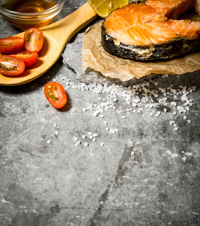 Grilled salmon with olive oil, tomatoes, lemon and spices. On the stone table.の写真素材