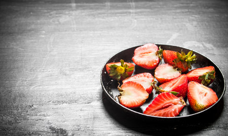 Halves of strawberry in the old plate. On the black wooden table.の写真素材