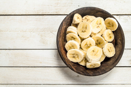 Sliced bananas in a wooden bowl. On a white wooden background.の写真素材
