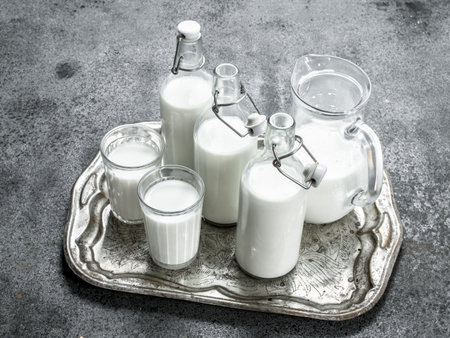 Fresh milk in bottles, jugs and glasses on a steel tray. On a rustic background.の写真素材