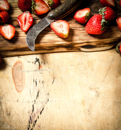 Sliced strawberries with the old knife on the Board. On wooden background.の写真素材