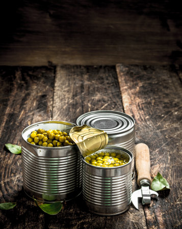 Canned green peas in a tin can with opener. On a wooden background.の写真素材