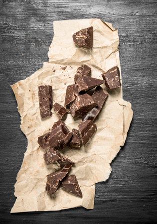Chunks of chocolate on old paper. On the black chalkboard.の写真素材