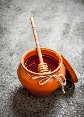 Fresh honey in a clay pot with a wooden spoon. On rustic background.の写真素材
