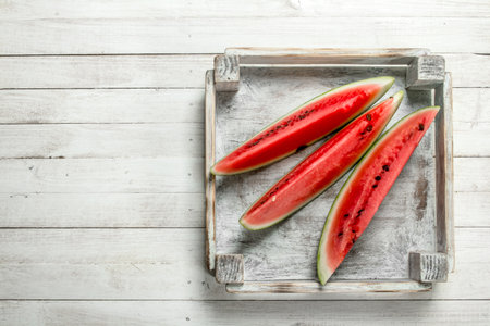 Pieces of sliced ripe watermelon in a box. On a white wooden table.の写真素材