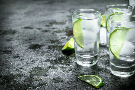 Vodka with pieces of lime and ice cubes. On a rustic backgroundの写真素材