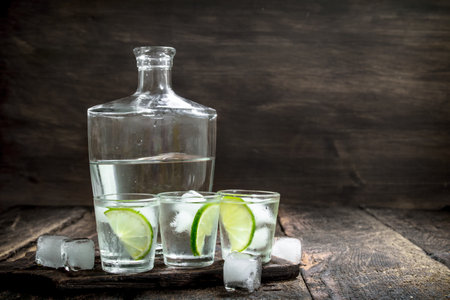 Vodka shots with lime and ice on the board. On a wooden background.の写真素材
