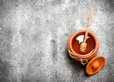 Fresh honey in a clay pot with a wooden spoon. On rustic background.の写真素材