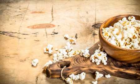 Popcorn in a wooden bowl on the Board. On a wooden table.の写真素材