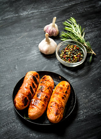 Fried sausages with garlic and herbs in a pan. On the black Board.の写真素材