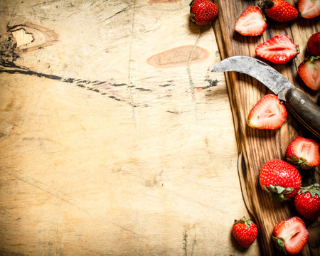 Sliced strawberries with the old knife on the Board. On wooden background.の写真素材