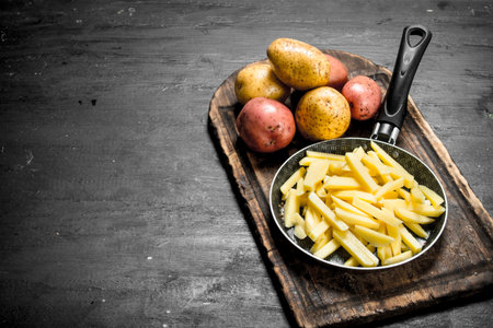 Sliced potatoes in an old frying pan. On the black chalkboard.の写真素材