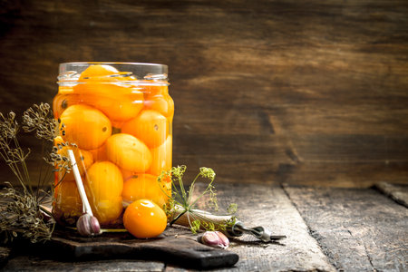 Pickled tomatoes with herbs and spices in jar. On a wooden background.の写真素材