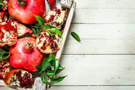 Ripe pomegranates with leaves in the box. On a white wooden table.の写真素材