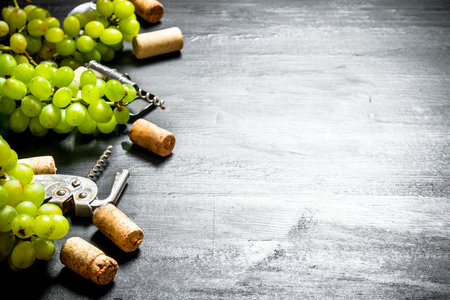 Wine corks with corkscrew and grape branch. On a black wooden background.の写真素材
