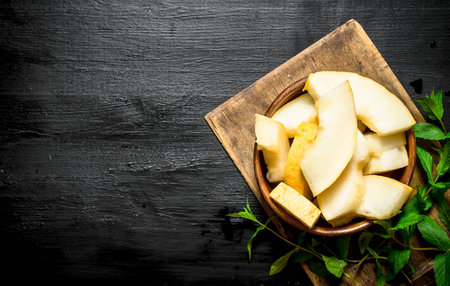 Sliced of ripe melon with fresh mint. On the black wooden table.