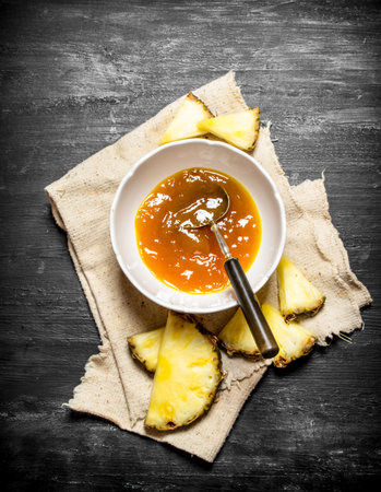 Pineapple jam in a dish with slices. On a black wooden background.の写真素材