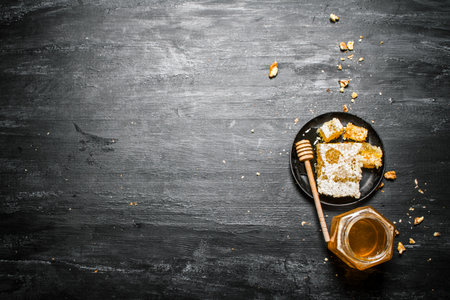 Honey style. A jar of natural honey and honey comb in the pan. On black rustic background.の写真素材