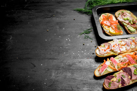 Sandwiches with bacon, salami, crab meat and vegetables. On the black chalkboard.