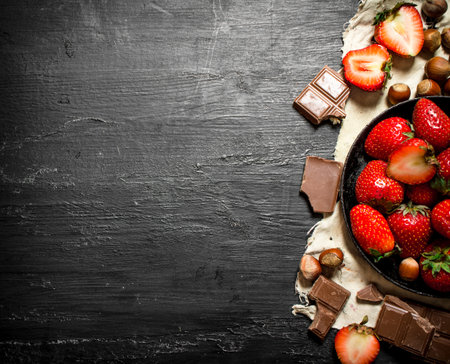 Strawberries with slices of chocolate and nuts. On the black wooden table.の写真素材