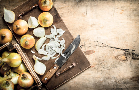 Slicing fresh onion on a cutting board with an old knife. On a wooden background.の写真素材