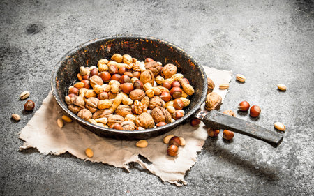 Different nuts in a frying pan. On rustic background.の写真素材