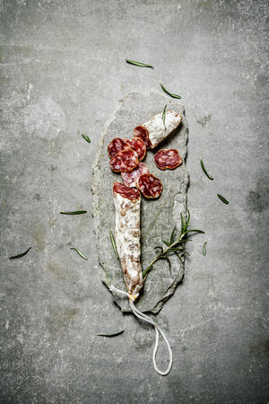 Sliced salami flavored with rosemary and spices. On a stone background.の写真素材