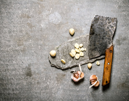 Chopped fresh garlic and old hatchet on a stone stand. On a stone background.の写真素材