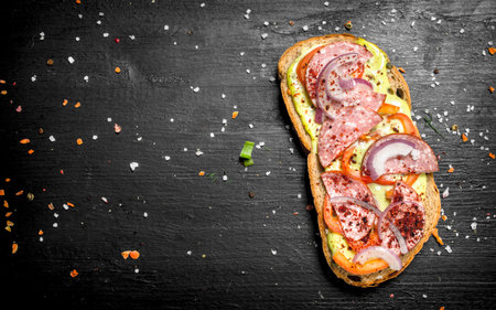 Sandwich with salami, tomatoes and red onion. On the black chalkboard.の写真素材