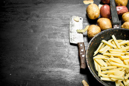 Sliced potatoes in an old frying pan. On the black chalkboard.の写真素材