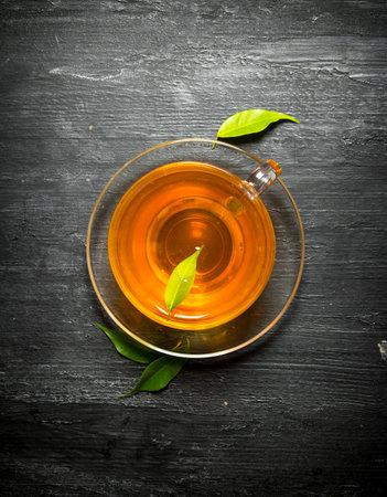 Cup of tea with green leaves. On a black wooden background.の写真素材