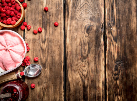 Raspberry jam with ice cream and wild berries. On a wooden table.の写真素材